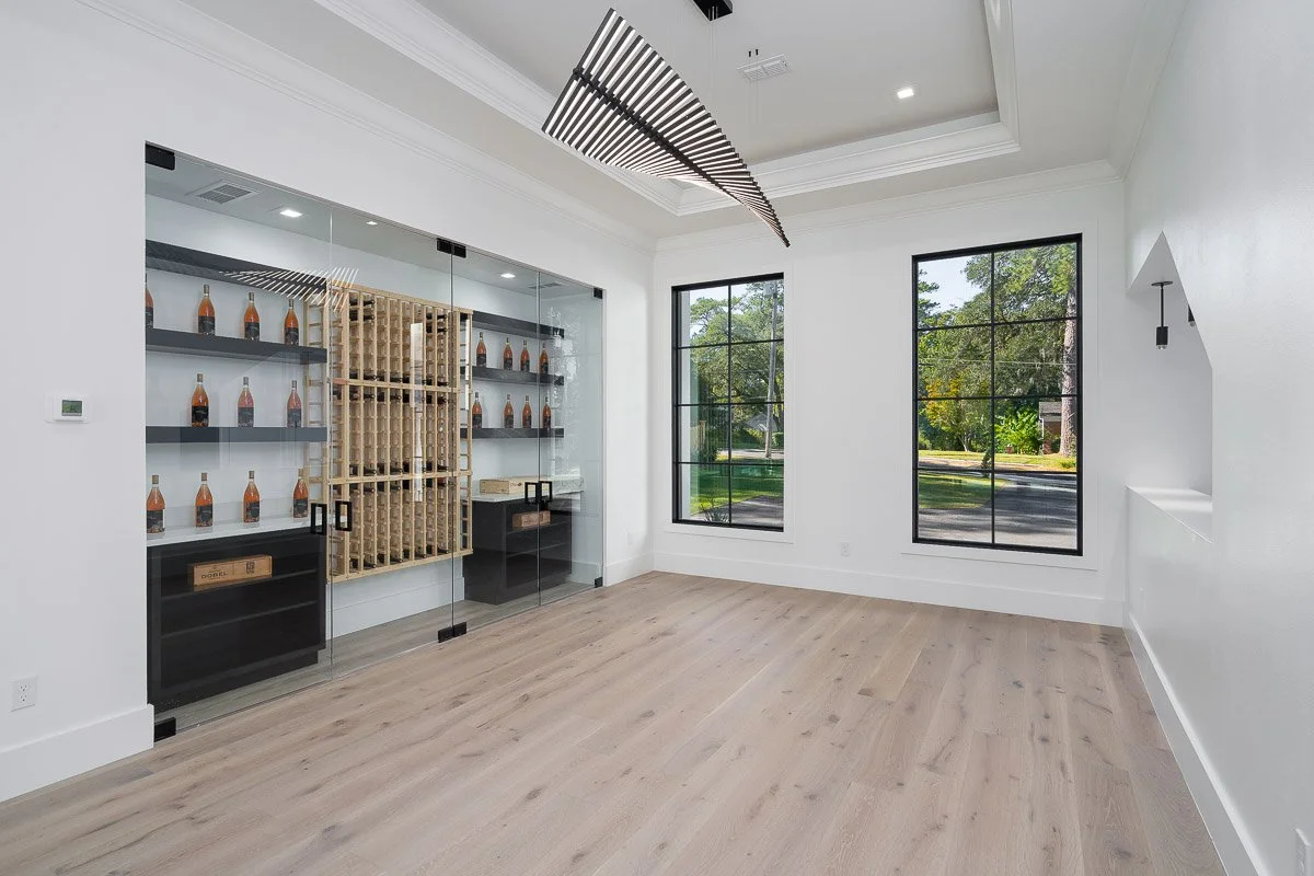 Empty room with large windows, light-colored wood flooring, and a glass-enclosed wine storage area.