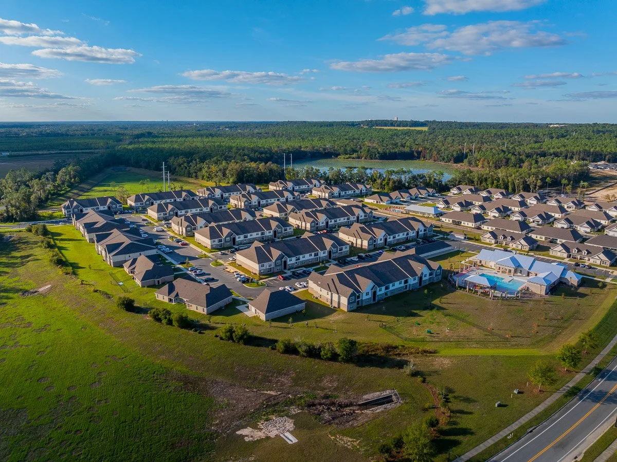 Aerial Real Estate photo of a residential housing development with multiple houses, a community swimming pool, and surrounding green spaces and trees.