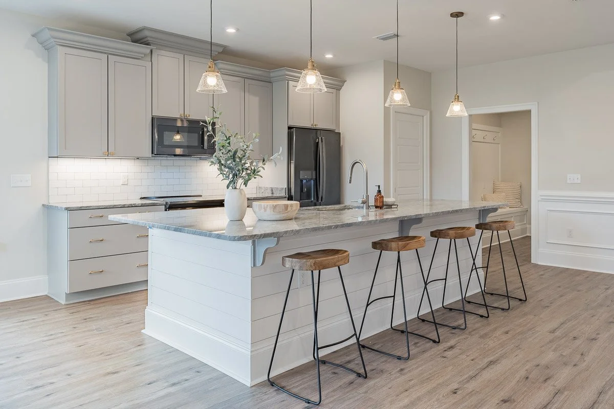 Real Estate photo of a modern kitchen with white cabinets, marble island, pendant lights, and four wooden barstools with metal legs