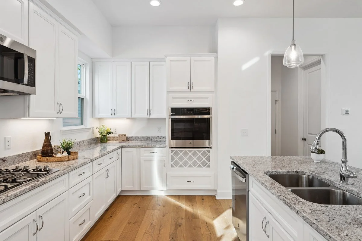 Real Estate photo of a white kitchen with granite countertops, stainless steel appliances, and hardwood floors.