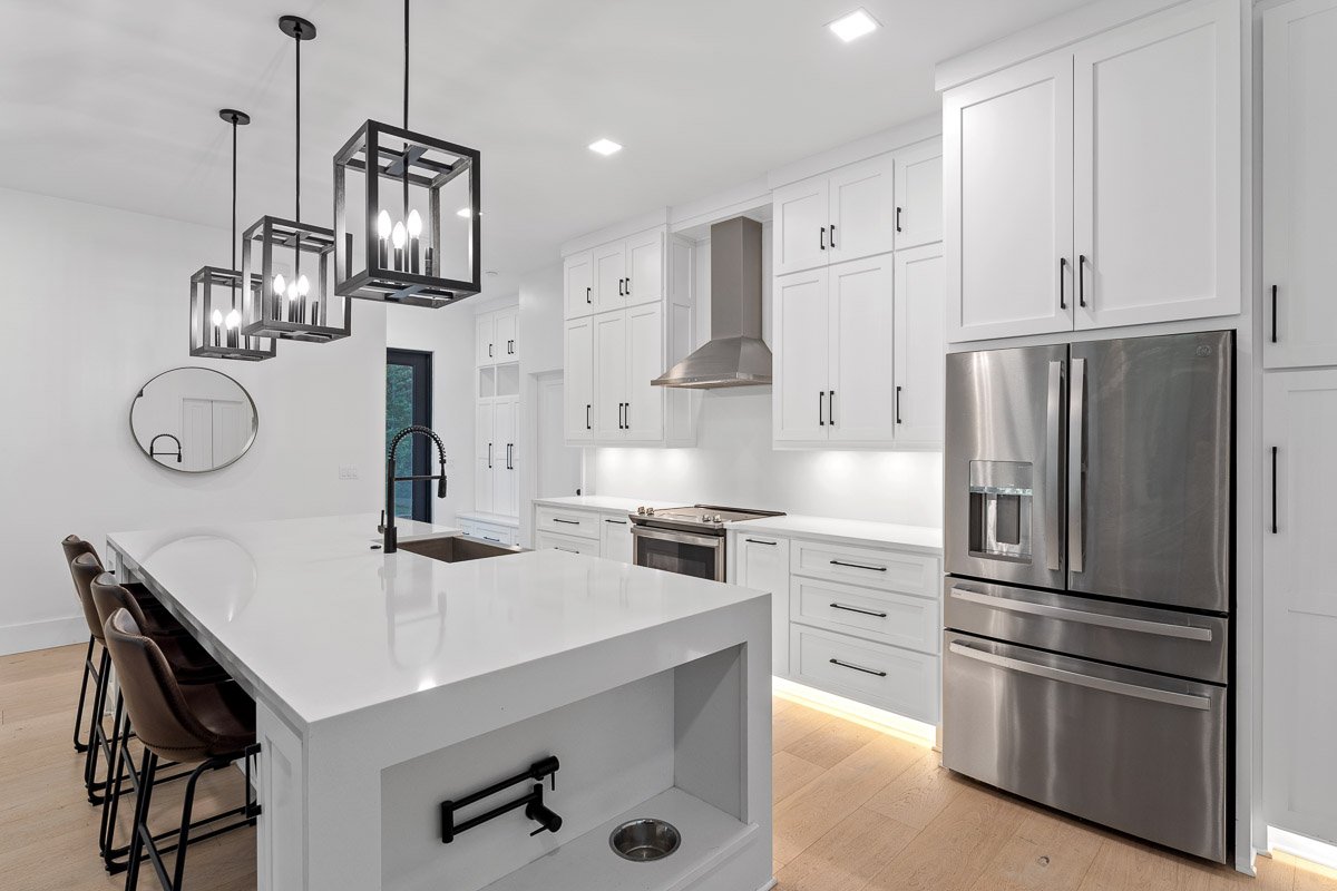 Real Estate photo of a modern white kitchen with stainless steel appliances, a large central island with bar stools, dog bowl nook, and pendant lighting.