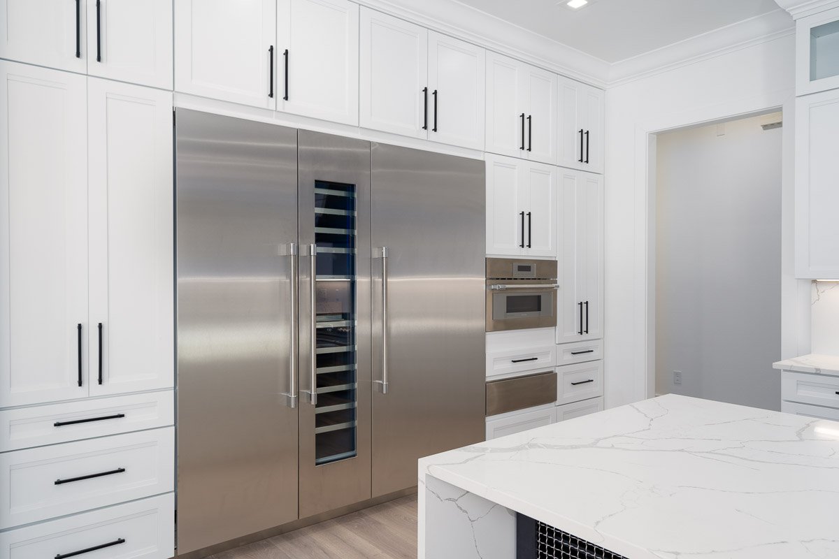 Modern kitchen with white cabinetry, stainless steel appliances including a refrigerator and built-in oven, and a white marble kitchen island.