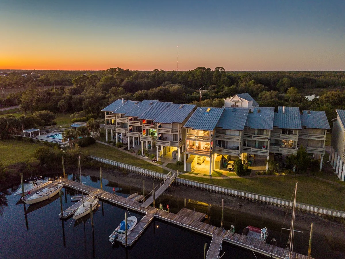 Aerial Real Estate photo of a waterfront condo with a dock and boats at dusk, surrounded by trees and greenery.