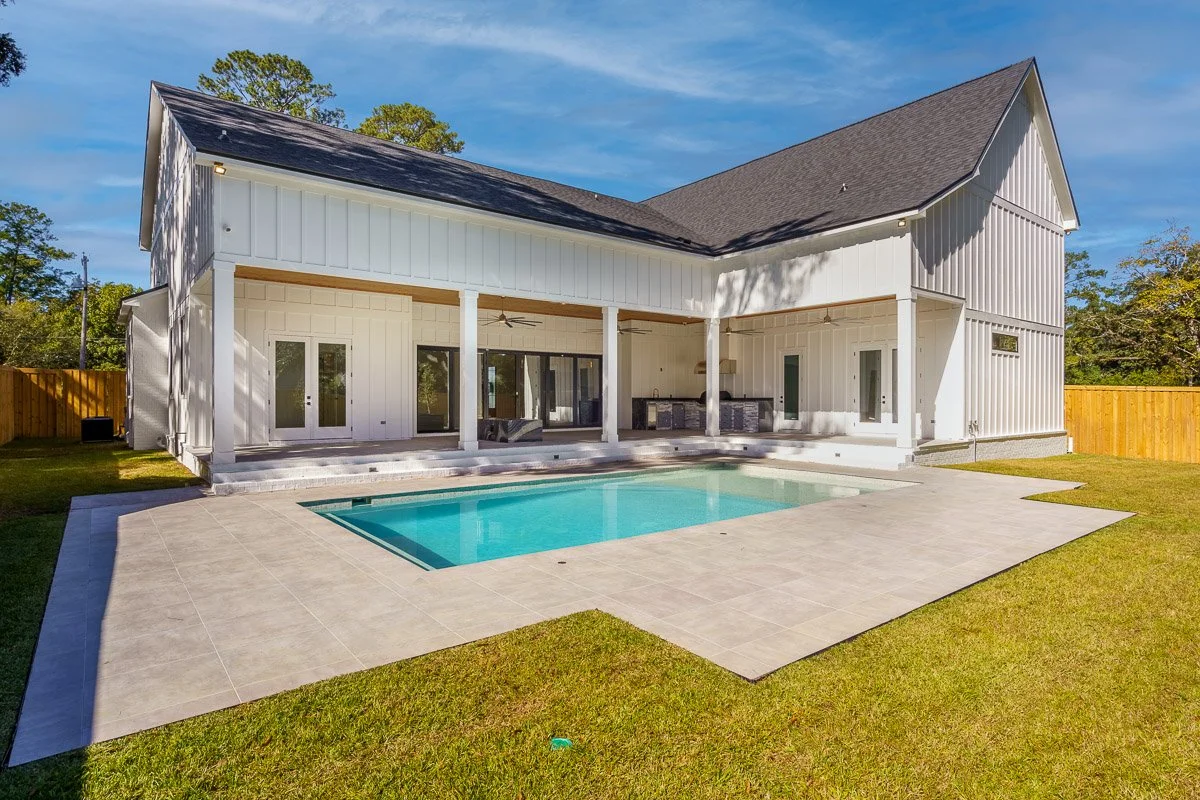 Backyard with a rectangular swimming pool, patio, and a large white house with a covered porch.