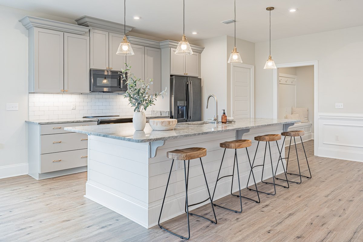 Real Estate photo of a modern kitchen with white cabinets, marble island, pendant lights, and four wooden barstools with metal legs