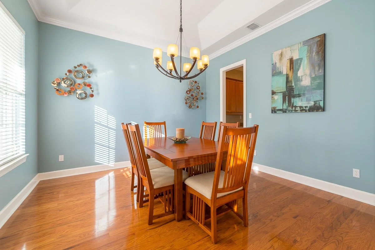 Real Estate photo of a dining room with a wooden table, six matching chairs, light blue walls, a chandelier, wall art, and hardwood floors.