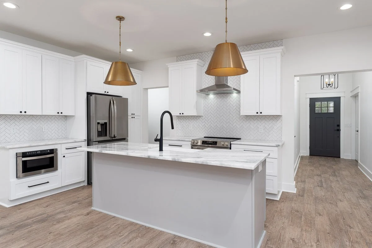 Modern kitchen with white cabinets, stainless steel appliances, a marble island, and gold pendant lights.