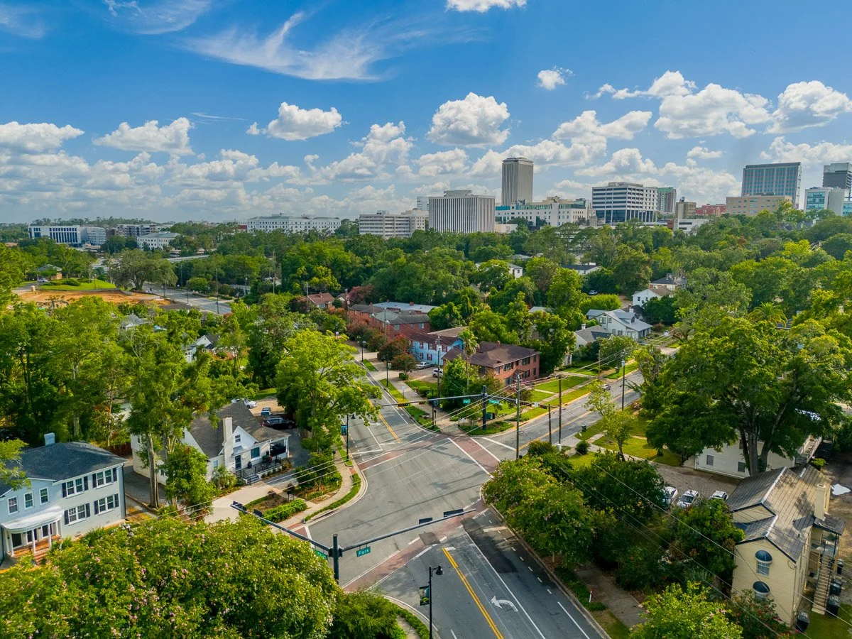 Aerial Real Estate photo of a home in a downtown area with trees, and tall office buildings under a partly cloudy sky.
