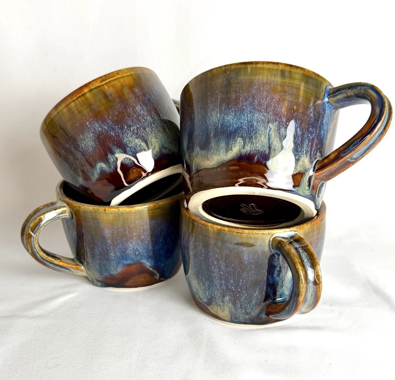 Four ceramic coffee mugs with multicolored glaze, arranged in a cluster on a white surface.