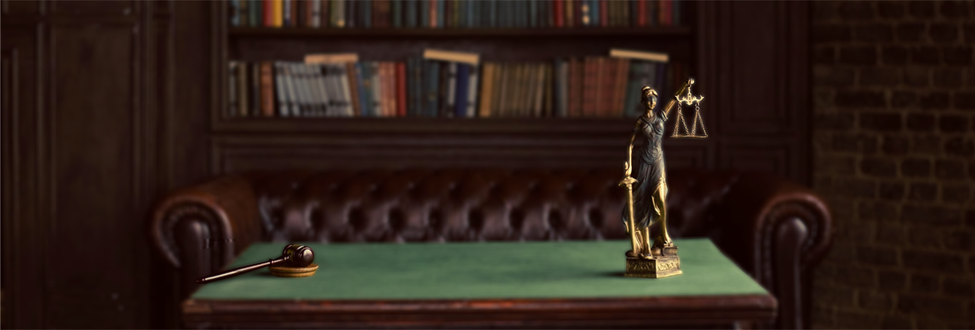 A judges' gavel, a brass Lady Justice statue holding scales, on a green table in a law office or library setting with leather sofa and bookshelf in background.