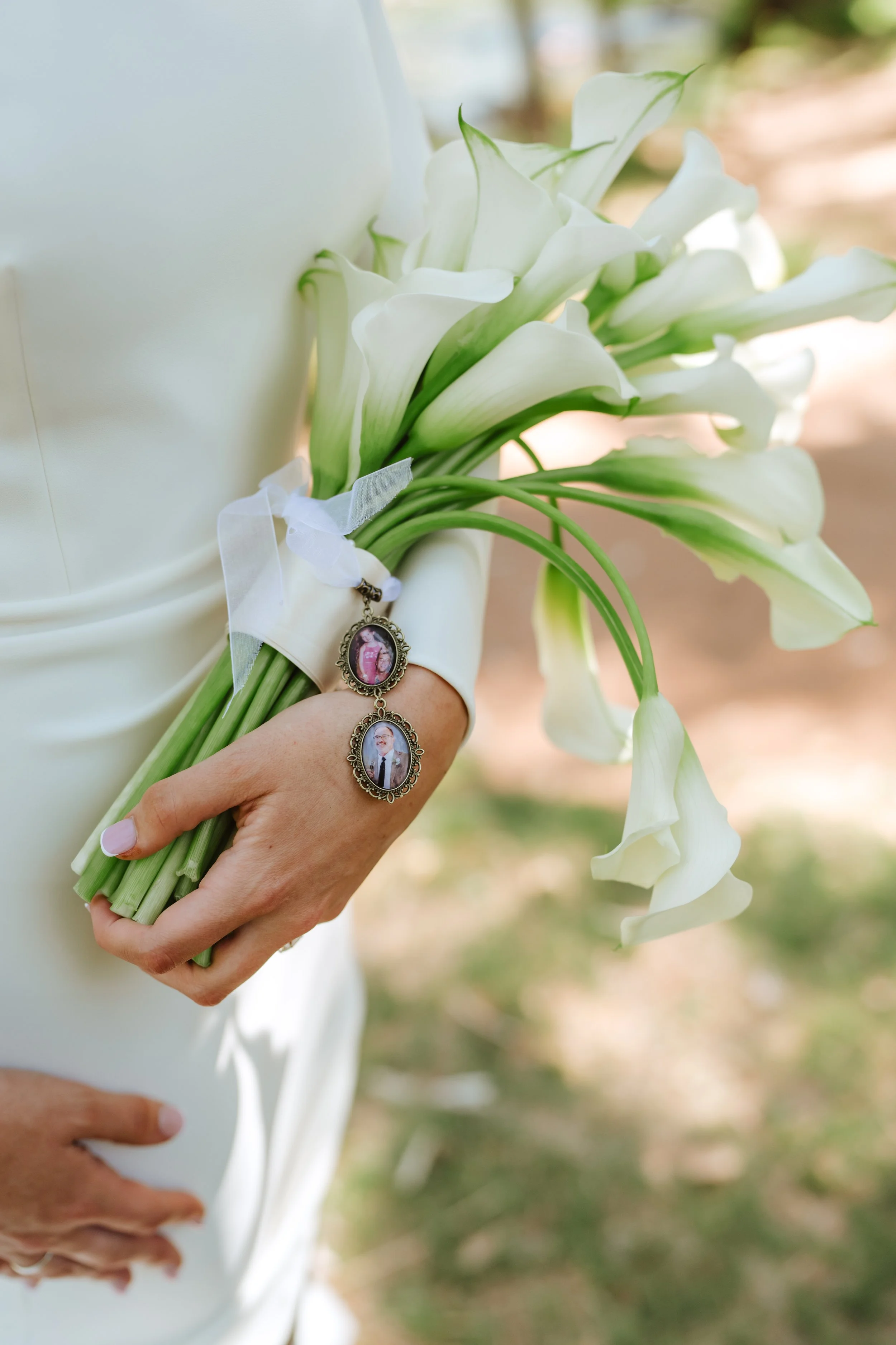 Person holding a bouquet of white calla lilies with a religious medal hanging from the stems.