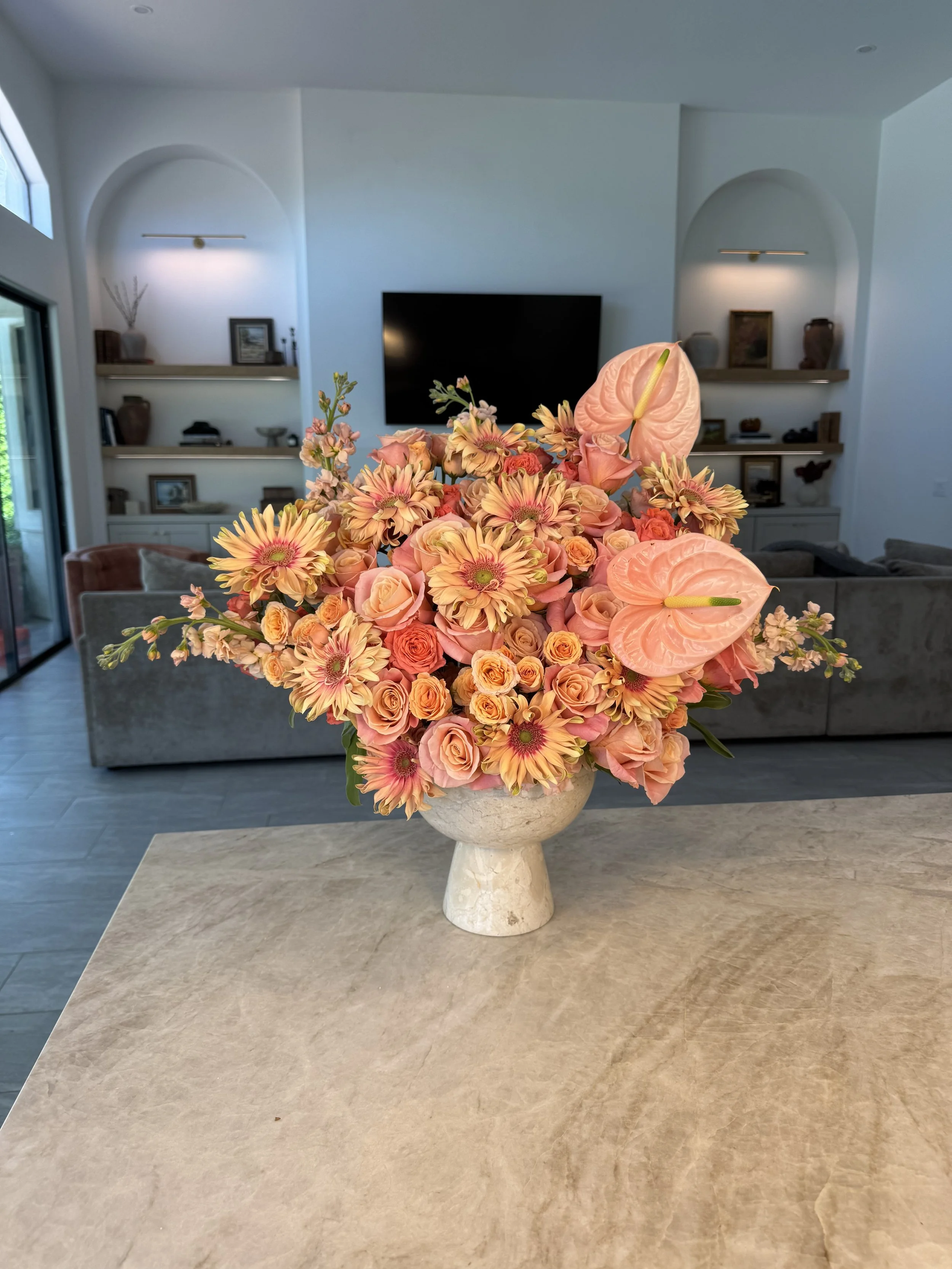 A large bouquet of pink and peach flowers in a beige vase on a wooden table in a living room.