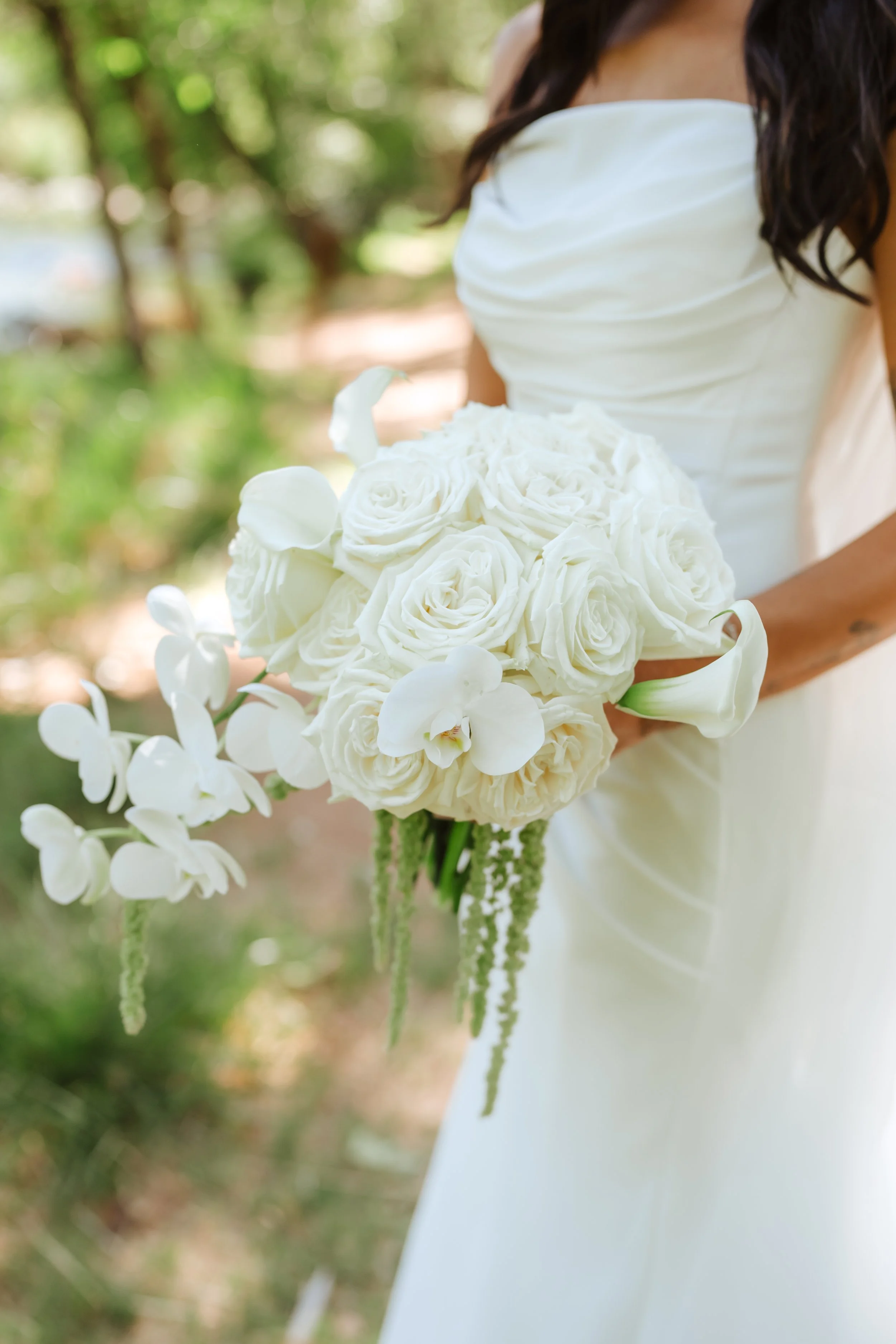 A woman in a white dress holding a bouquet of white roses and orchids outdoors.
