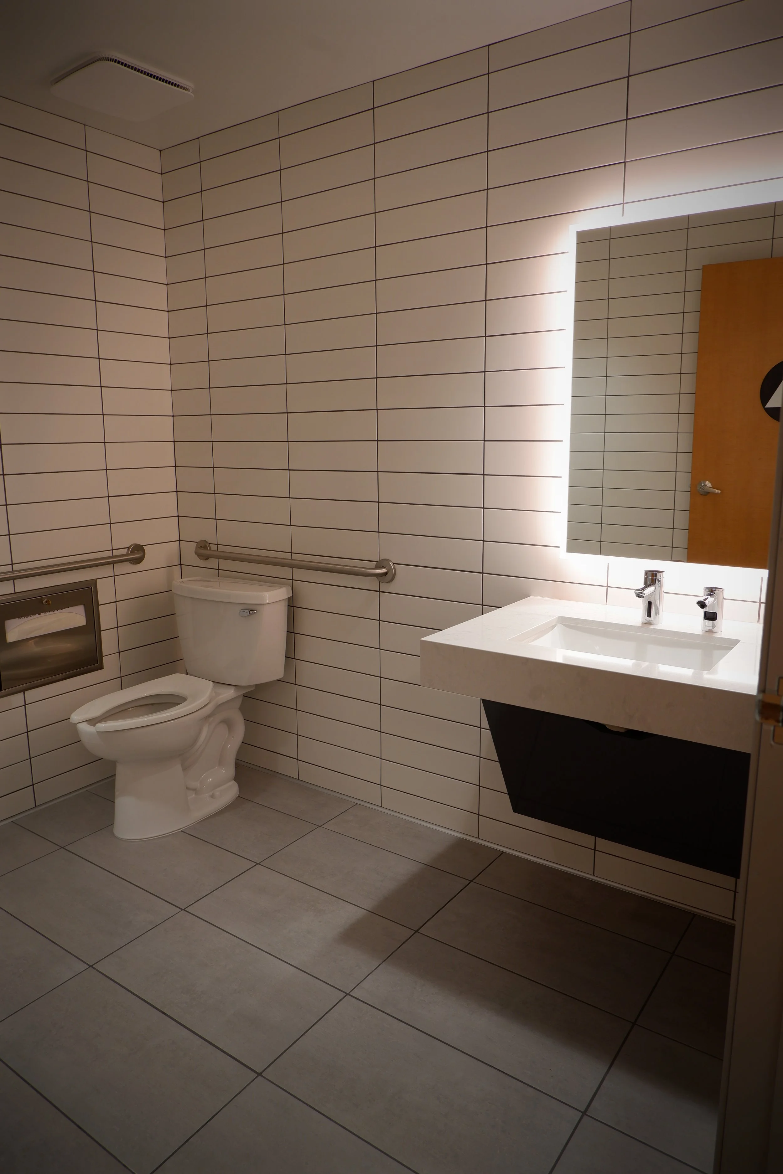 ADA-compliant commercial restroom with wall-hung sink, toilet and grab bars plumbed by Kuehnel Plumbing