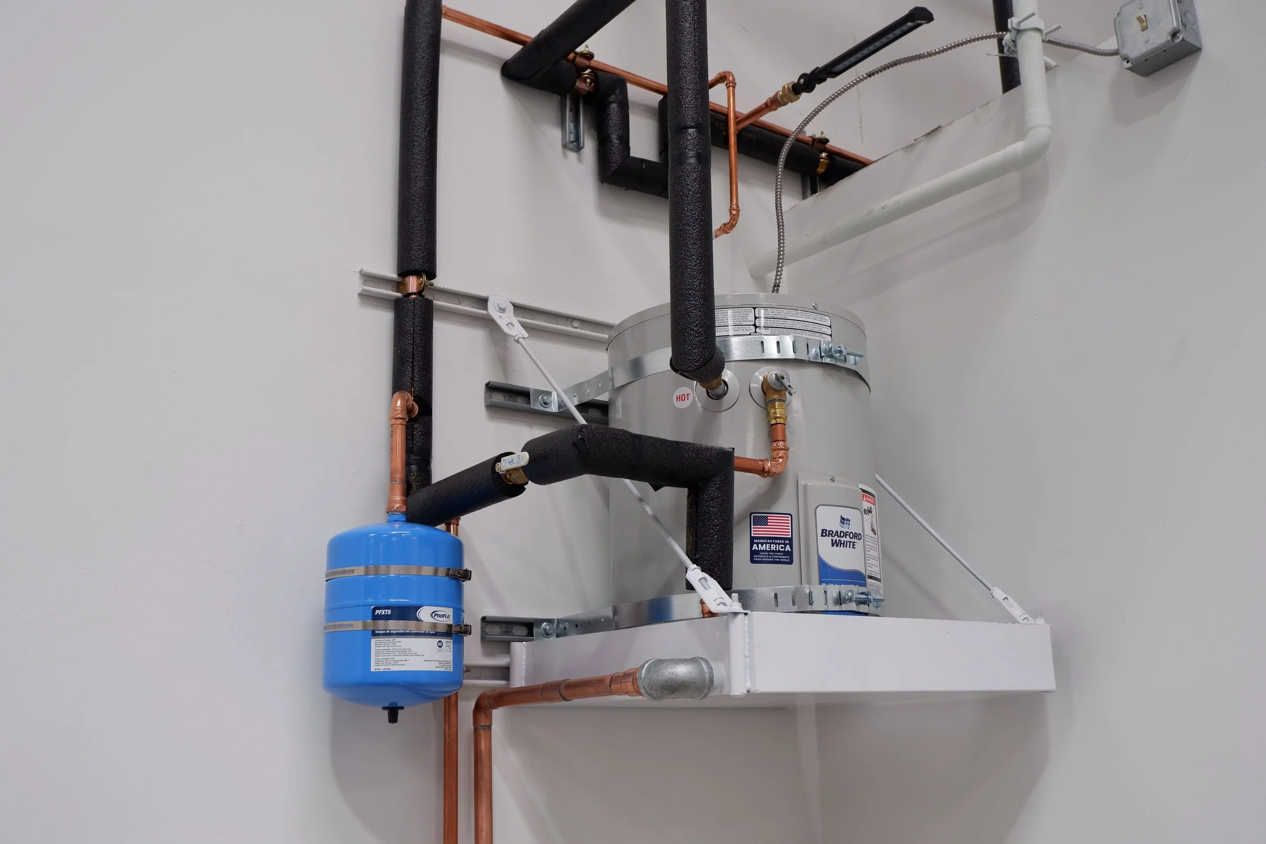 Wall-mounted water heater with expansion tank and insulated copper piping installed by Kuehnel Plumbing