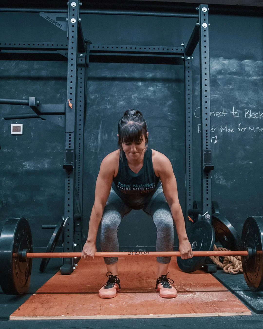 A woman in workout clothes performing a deadlift with a barbell in a gym.