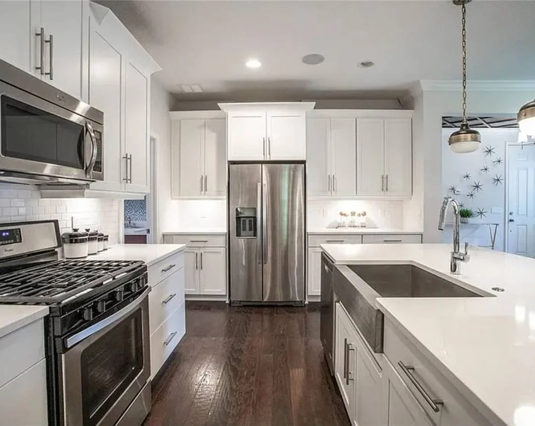 Modern kitchen with white cabinets, stainless steel appliances, a dark hardwood floor, and a large kitchen island with a built-in sink.