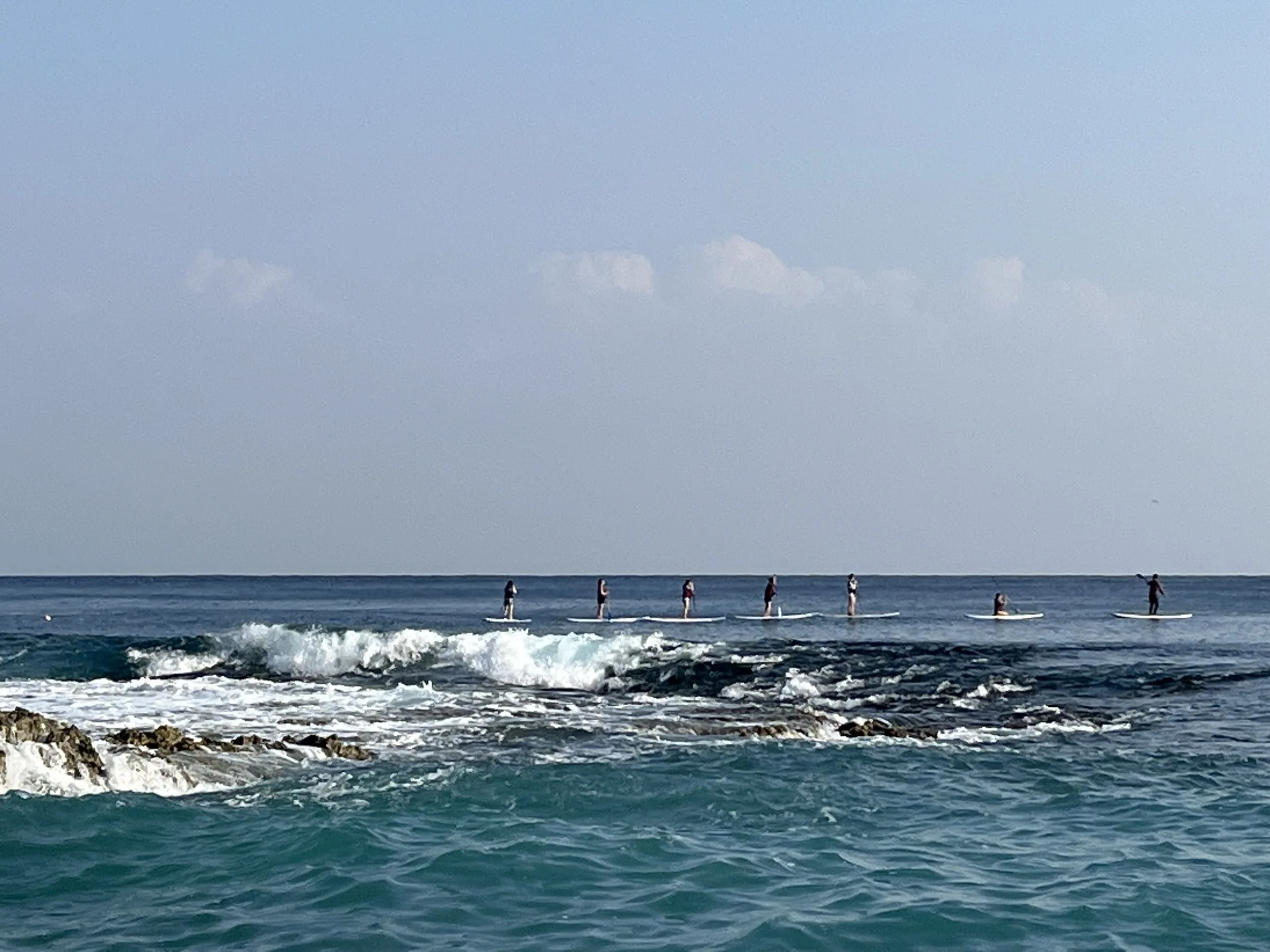 Group of seven people paddleboarding on the ocean near a rocky shoreline.