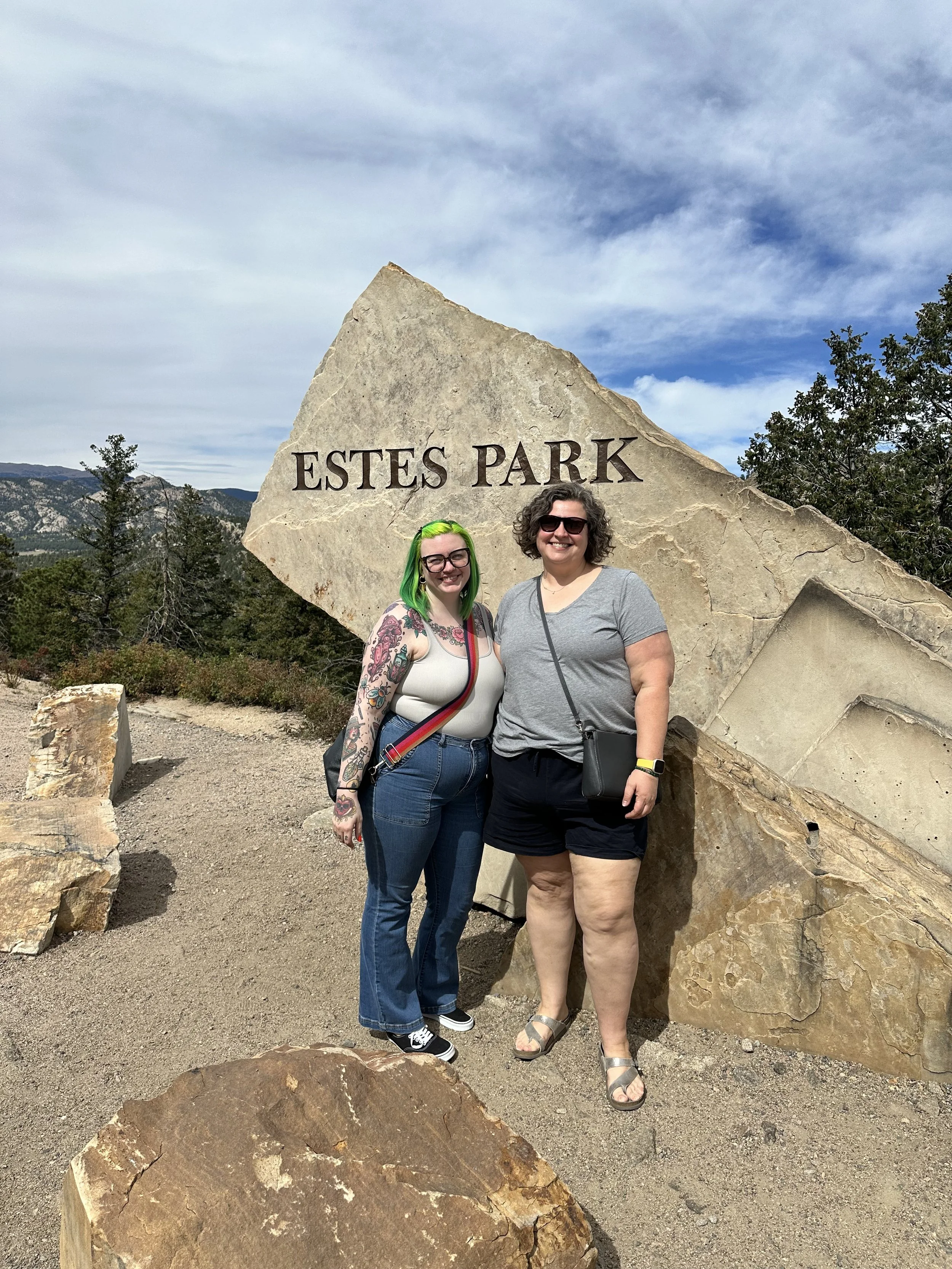 Nicole and Kristina standing in front of a large rock  with trees and mountains in the background.