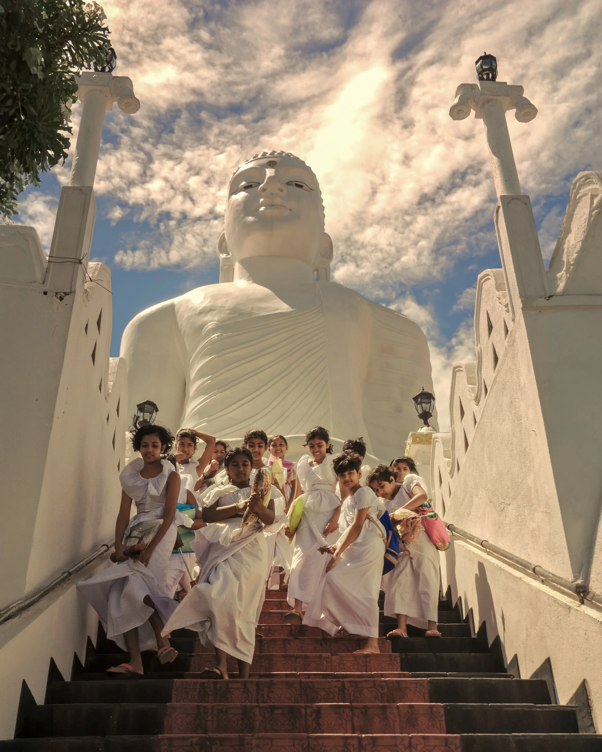Descent · Kandy · 2024 | Schoolchildren in white pour down the temple steps beneath the Bahiravokanda Buddha — a moment of noise and movement against something ancient and still.