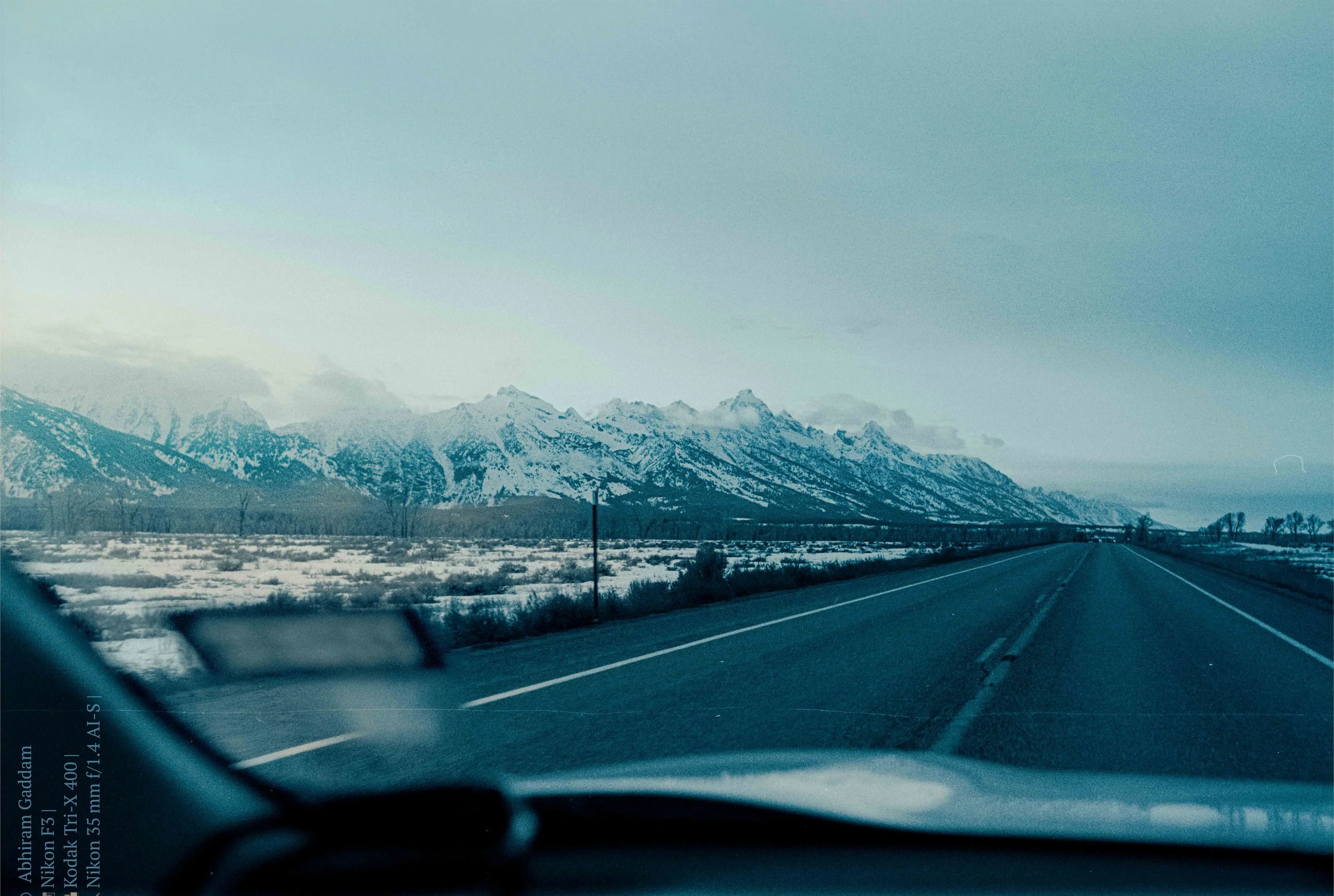 Teton Bound · Wyoming · 2024 | Shot through the windshield on Kodak Tri-X 400 — the range appearing as the road disappears into it.