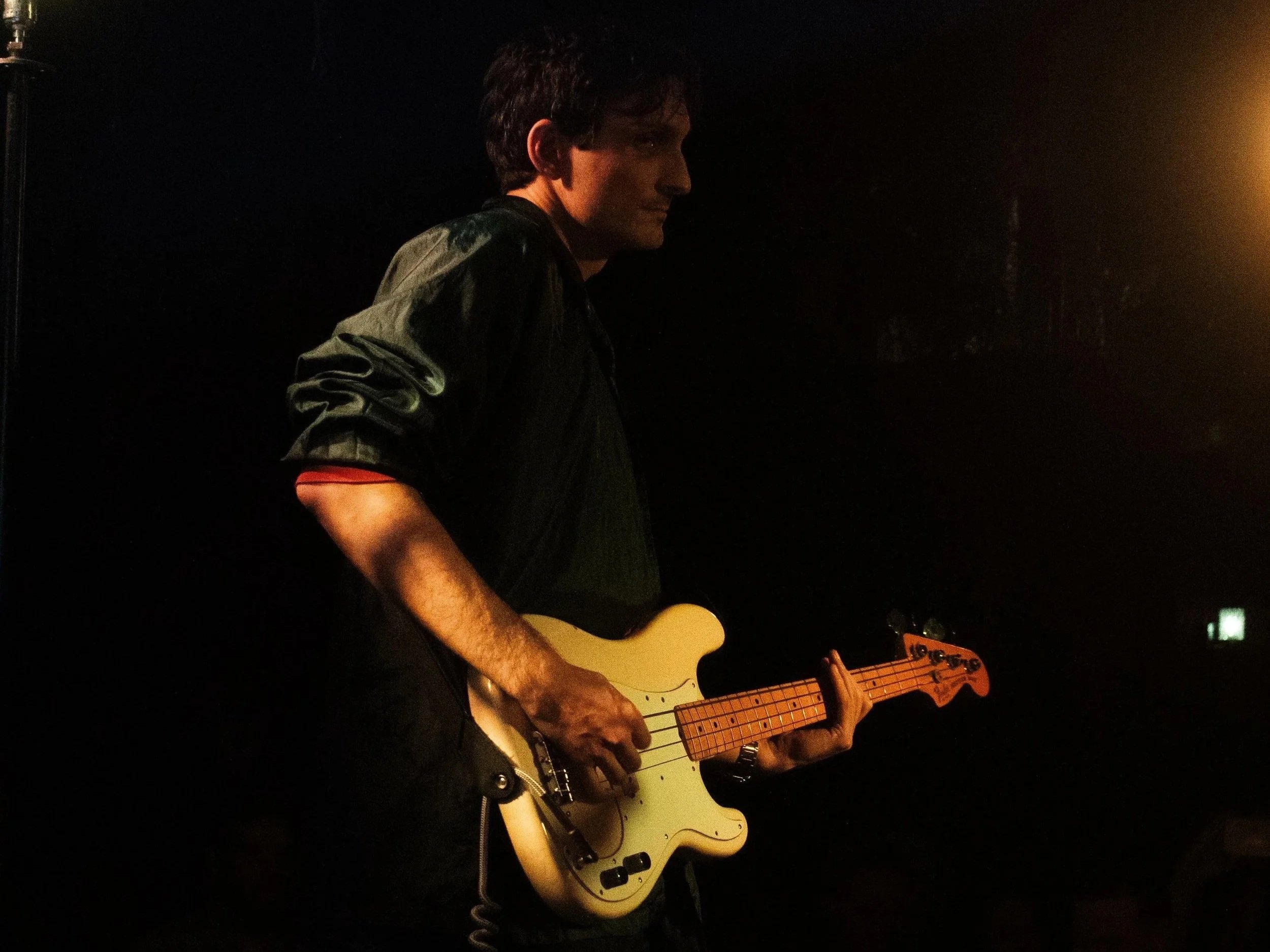 A man holding a yellow electric guitar in a dimly lit dark room.