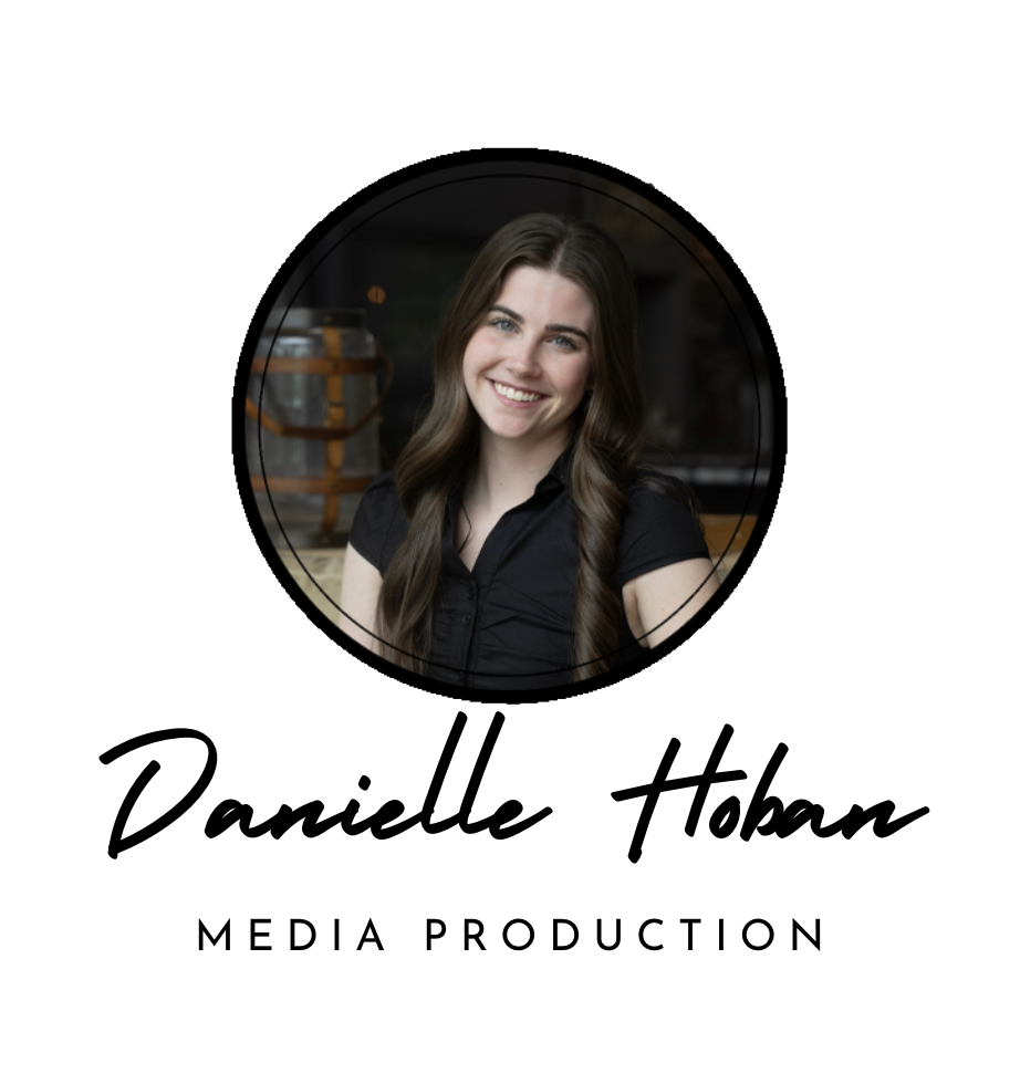 A woman with long dark hair, smiling, wearing a black shirt, in front of a dark background with a large jar.