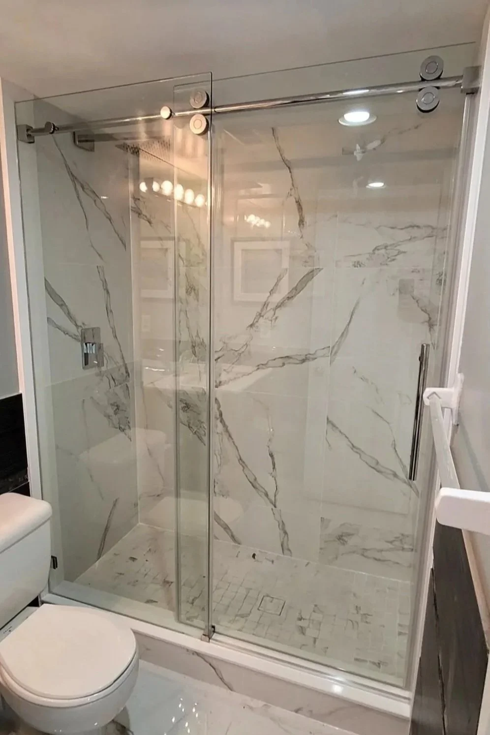 Modern bathroom shower with marble tile walls and glass doors, adjacent to a toilet.