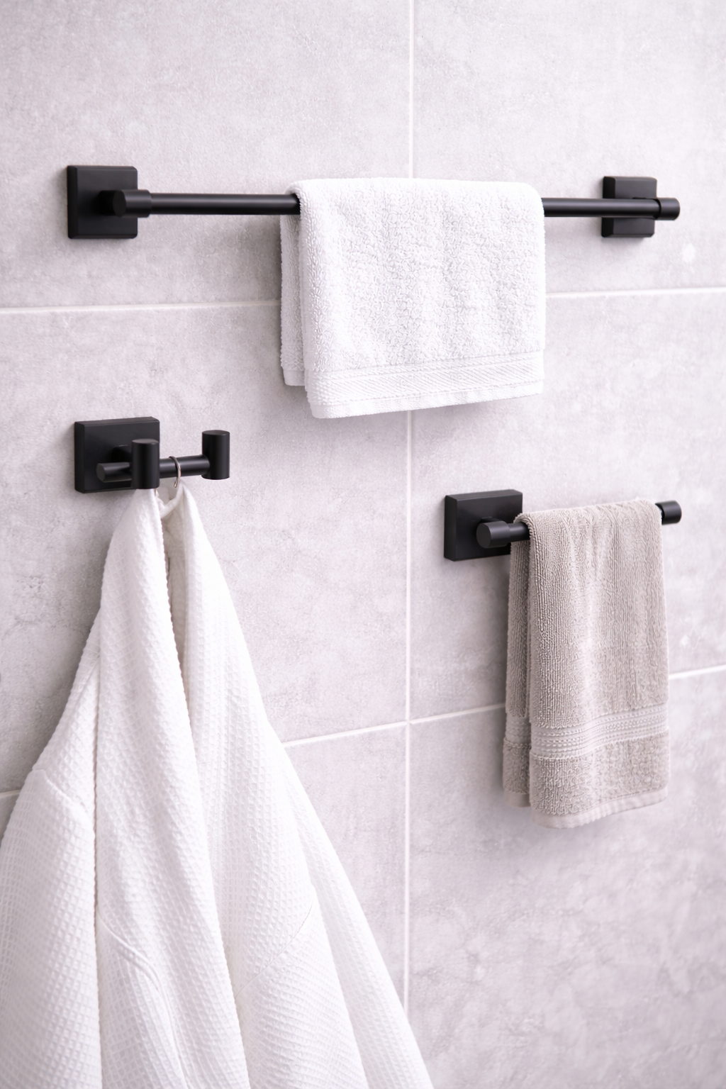 Bathroom wall with black towel racks holding white and beige towels, and a white robe hanging on a hook.