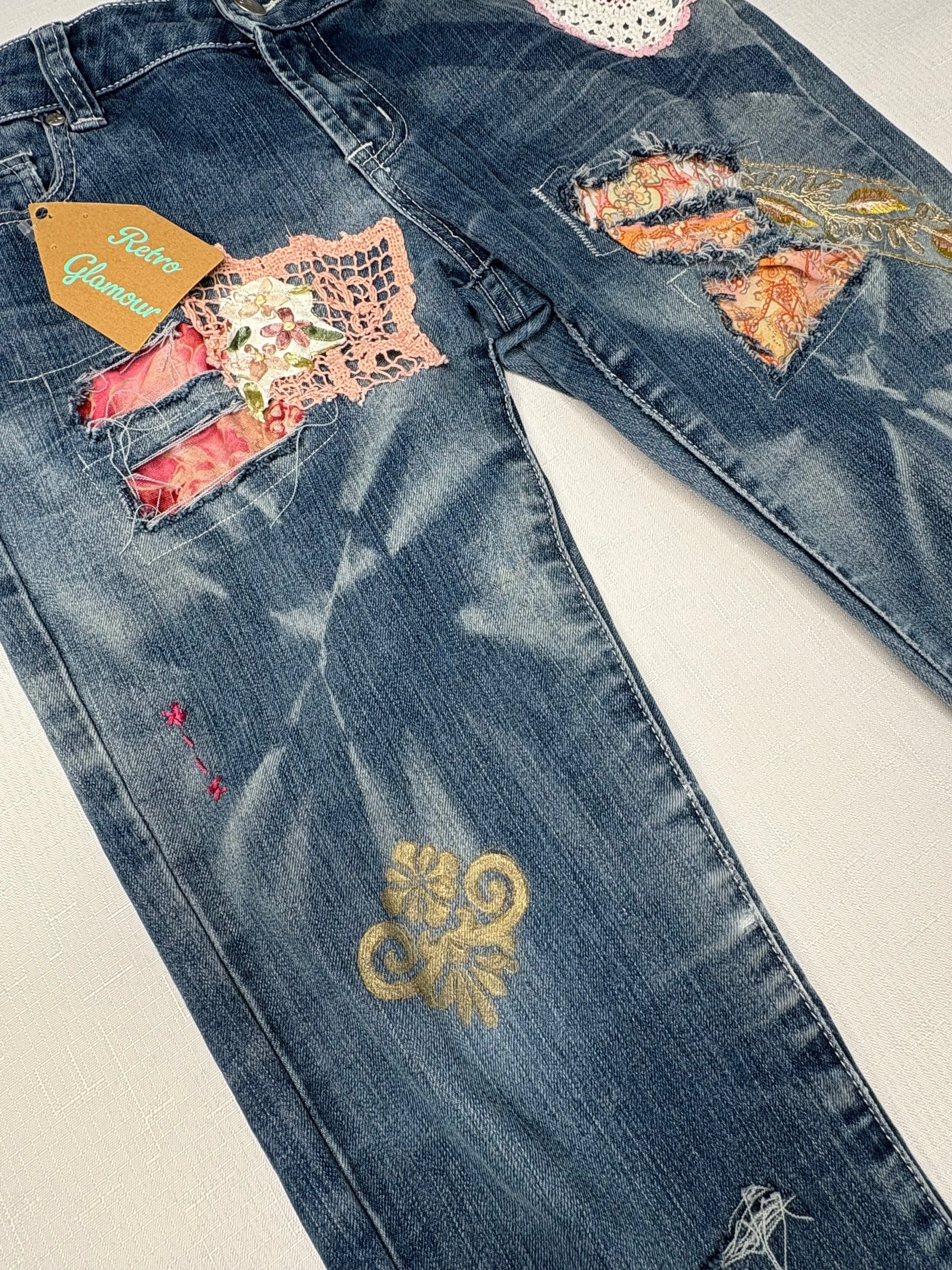 Pair of distressed blue jeans with vintage and floral embroidery, lace patches, and a "Retro Glamour" tag.