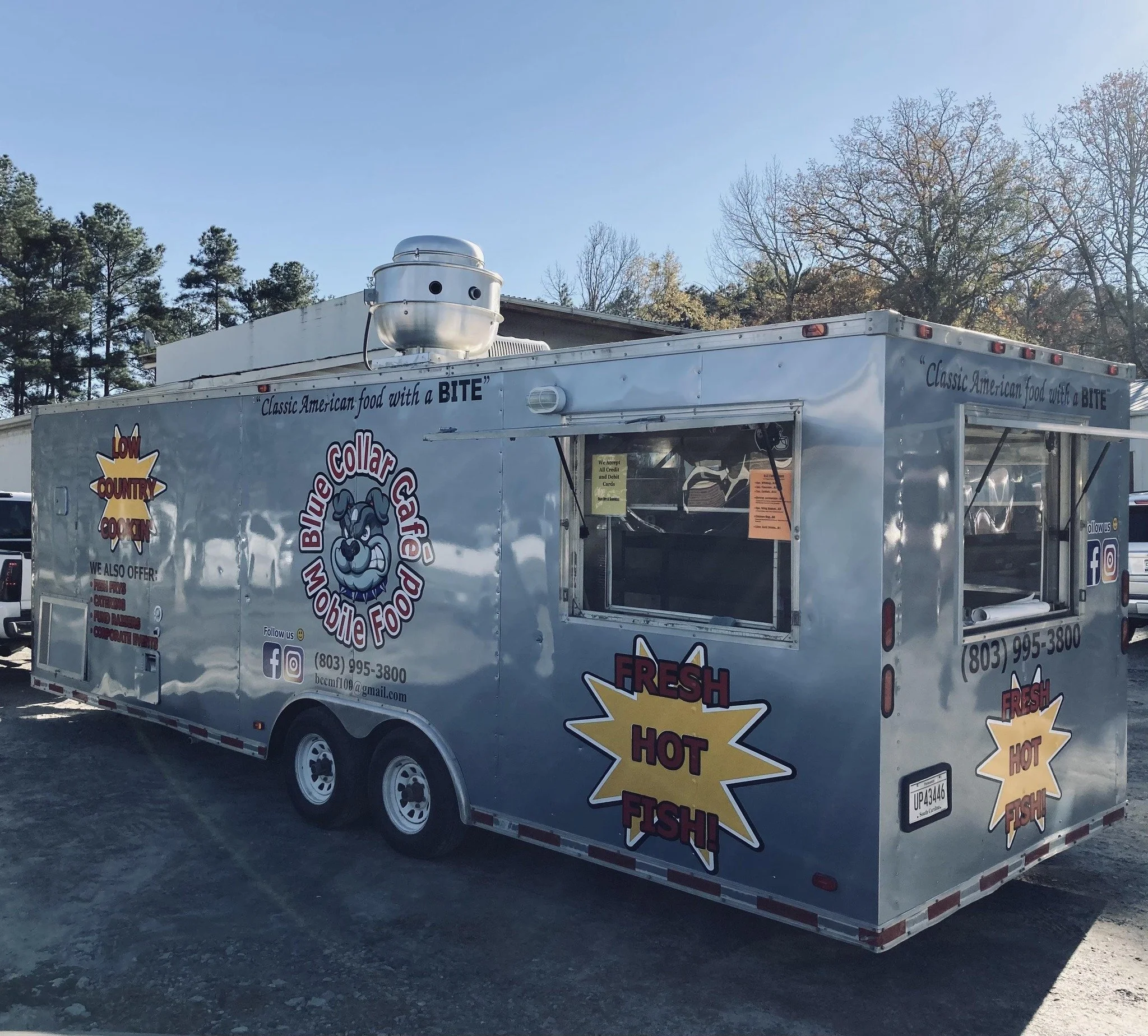 A food truck named Blue Collar Cafe Mobile Food offering fresh hot fish, with slogans like "Classic American food with a BITE" and "Low Country Cookin',' featuring a cartoon fish logo on the side.