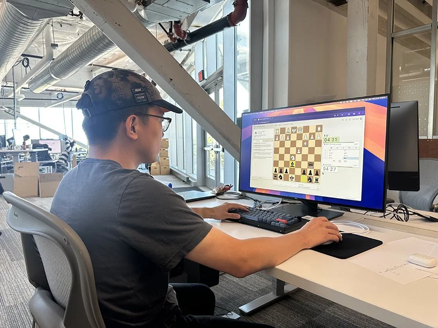 Person playing online chess on a computer in a modern office space.