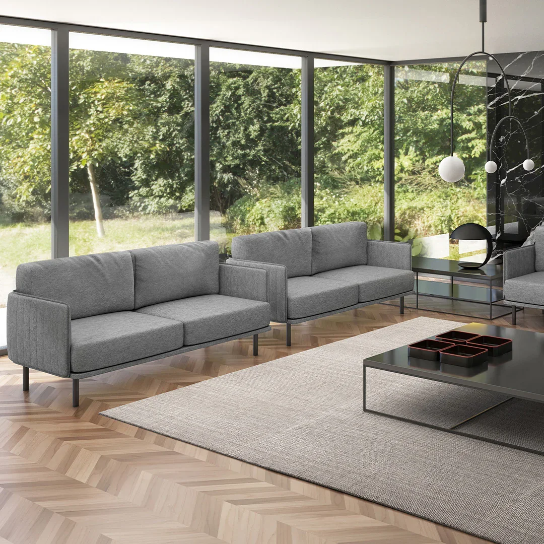 Sala moderna con sillones grises, mesa de centro negra, alfombra beige y ventanas grandes con vista a un jardín con árboles