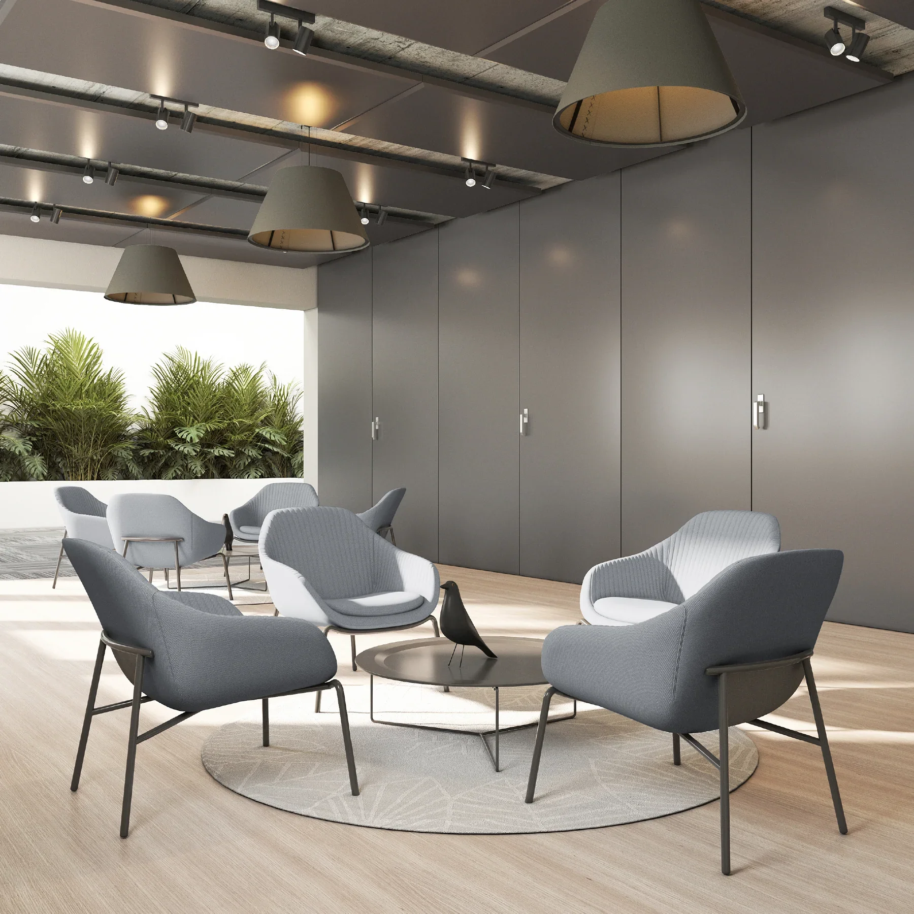Sala de reuniones moderna con sillas blancas y grises en círculo, mesa de centro con ave de escultura, paredes grises, techo expuesto y ventanal con plantas verdes afuera.