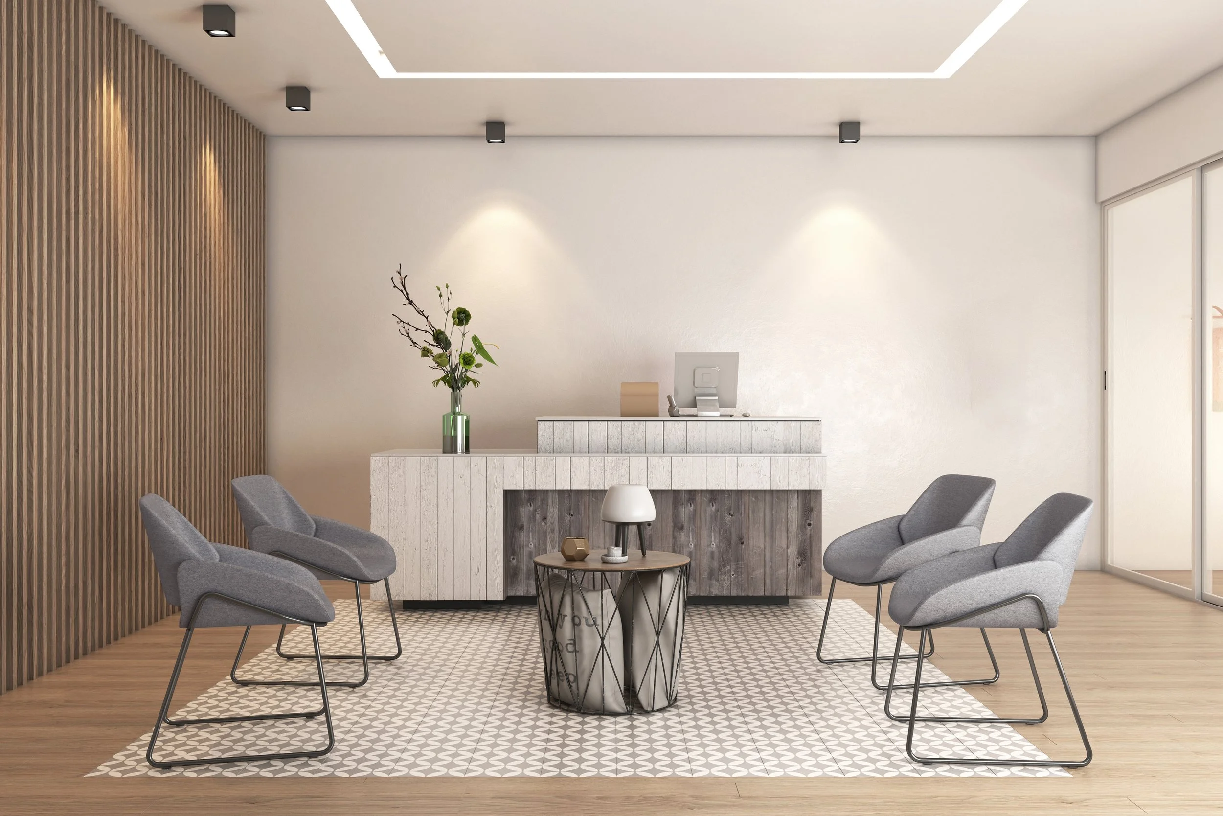 Sala de espera moderna con seis sillas grises alrededor de una mesa con lámpara, sobre un tapete de patrones blancos y grises, en un espacio con paredes blancas y una pared decorativa de madera, y un mostrador de recepción con planta y objetos decora