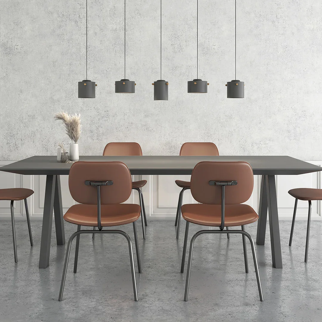 Mesa de comedor rectangular de color gris con cinco sillas de respaldo en tonos marrón y patas negras, y cinco lámparas negras colgantes en el techo, en un fondo de pared de color gris claro con textura.