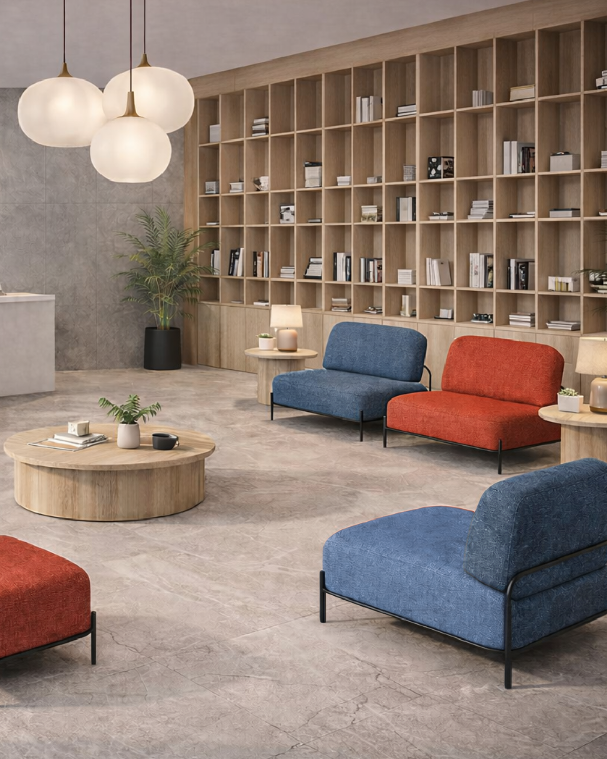 Sala de espera moderna con sillones azules y rojos, mesa de centro de madera, librero grande con libros y plantas decorativas, lámparas de mesa y de techo, paredes de piedra y suelo de mármol en tonos neutros.