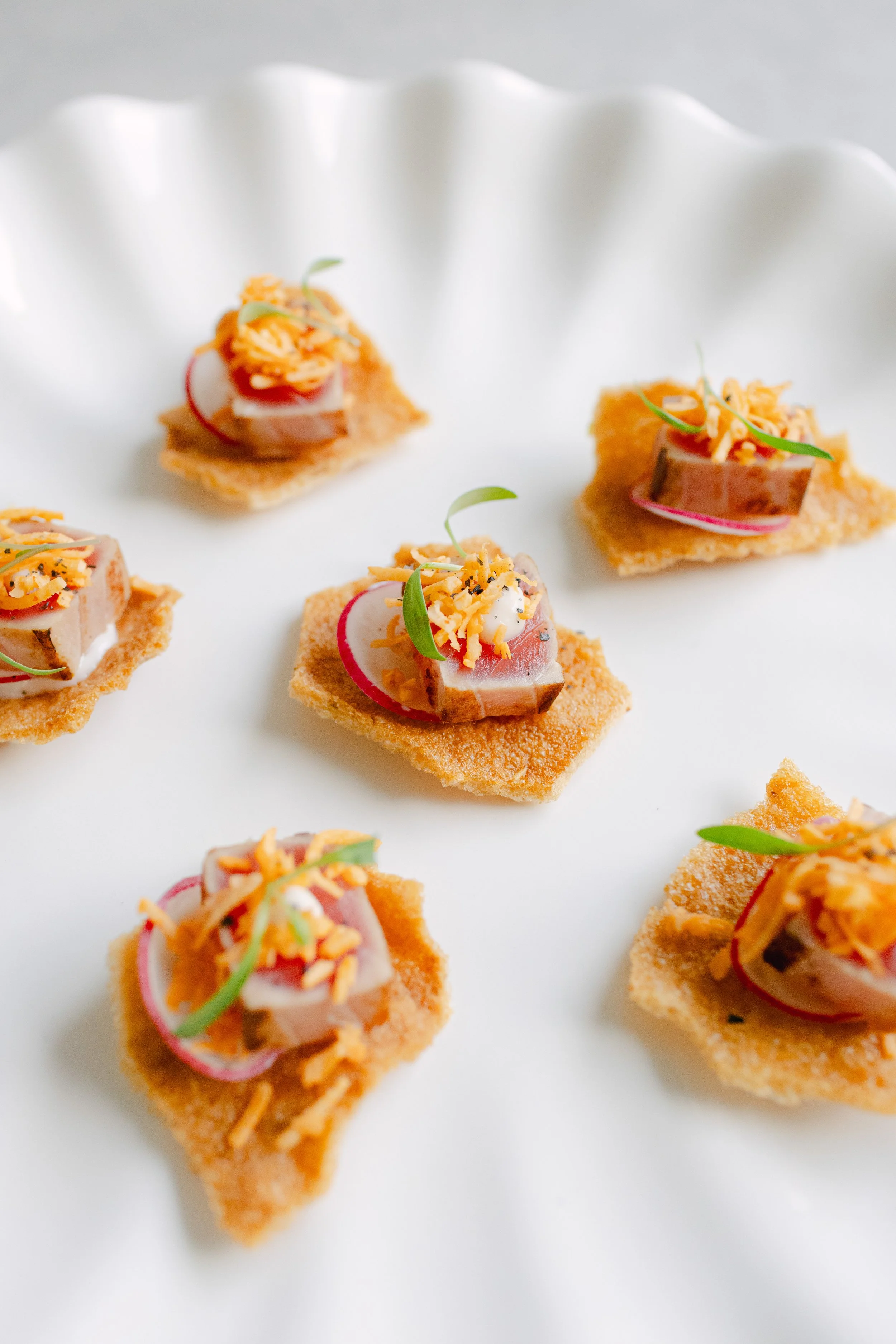 Canapés topped with sliced radish, shredded cheese, and microgreens on small crispy bread pieces.