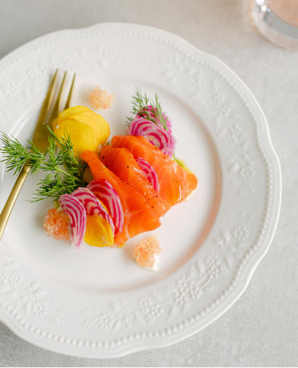 Sashimi slices of salmon and yellowtail with garnishes of radish, herbs, and ginger on an elegant white plate.