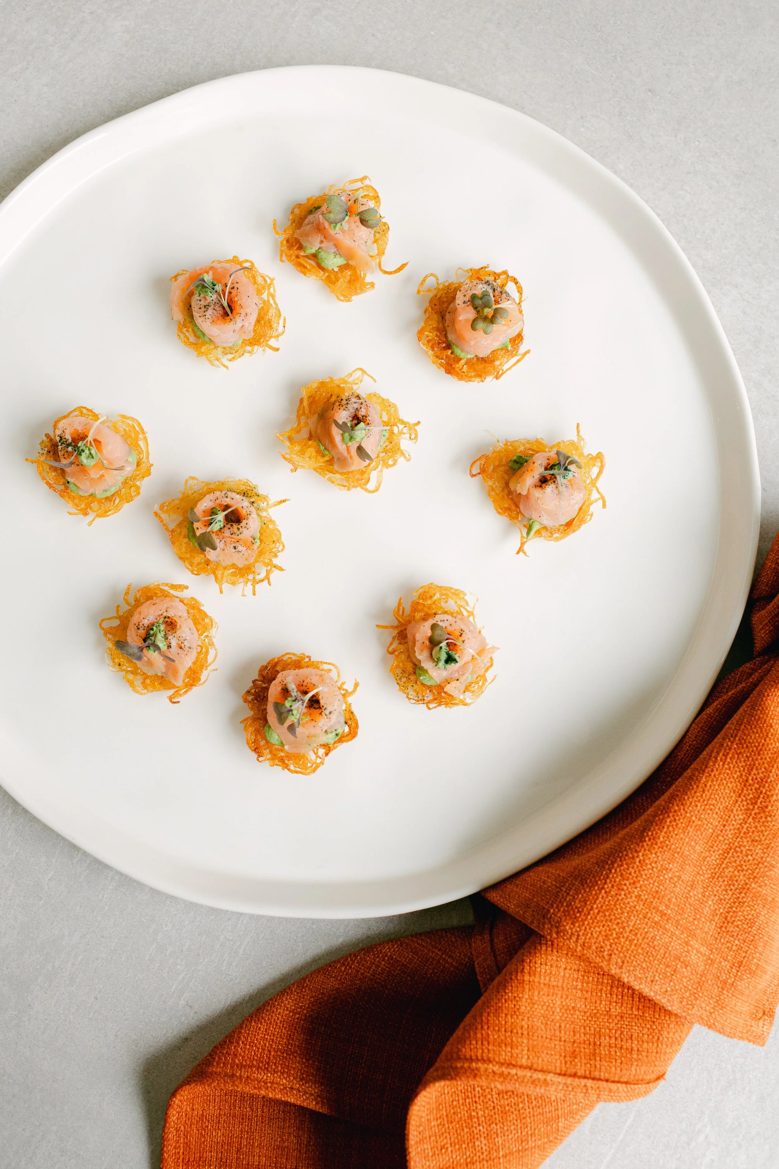 Small gourmet appetizers with pink topping, garnished with microgreens, on a white plate