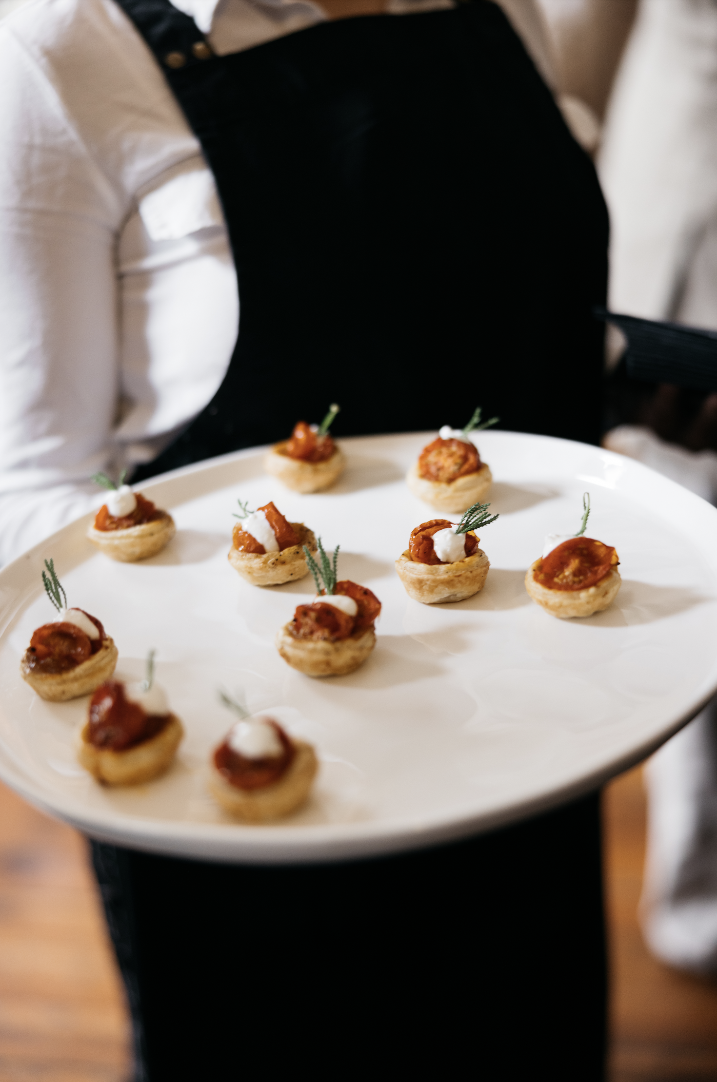 A server holding a platter with small savory appetizers topped with dollops of sauce and garnished with herbs.