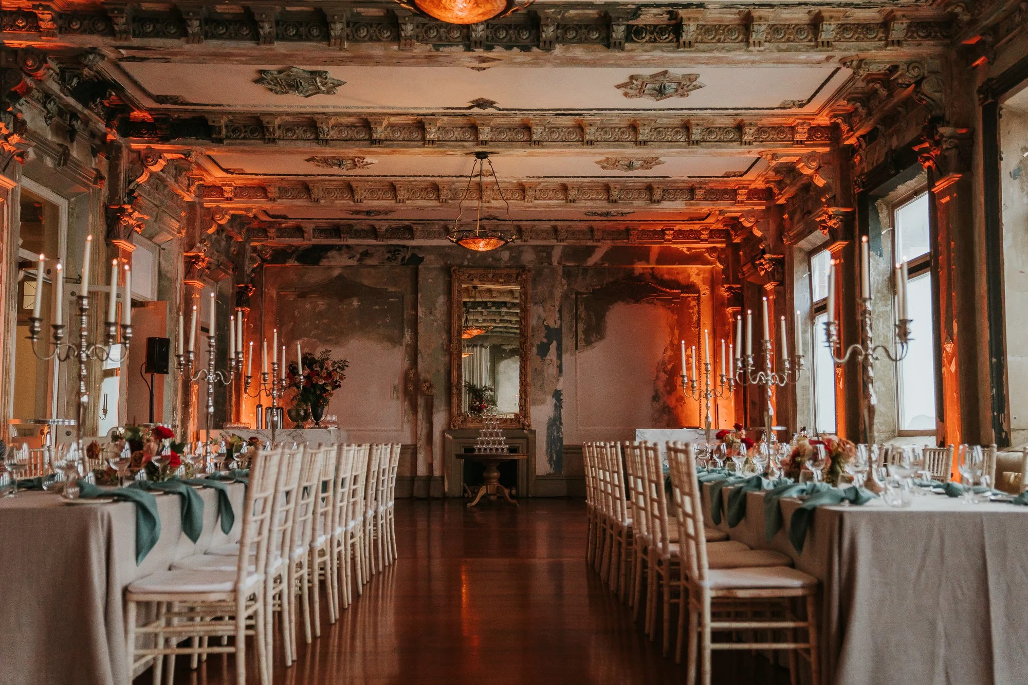 Elegant dining room with long rectangular tables, white chairs, tall candelabras, floral centerpieces, and ornate moldings on the ceiling, the george ballroom event space.