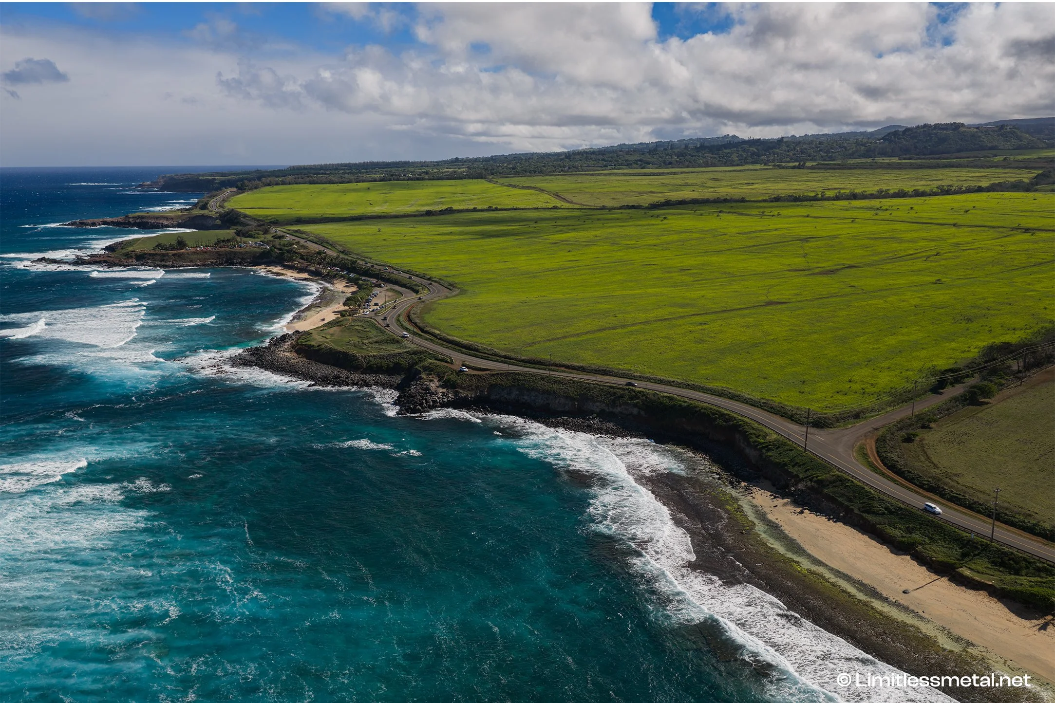 This aerial drone photograph captures the dramatic northeast shore of Maui, where turquoise Pacific waters meet rugged lava rock cliffs and a winding coastal road cuts through lush green landscapes. Printed on premium fine art mediums such as metal, 