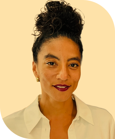 Portrait of a woman with curly hair styled in a high bun, wearing a white collared shirt and gold earrings, smiling slightly against a plain light background.