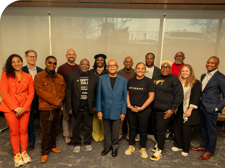 Group of 14 people standing together in a room for a photo, some smiling, dressed in casual and business attire.