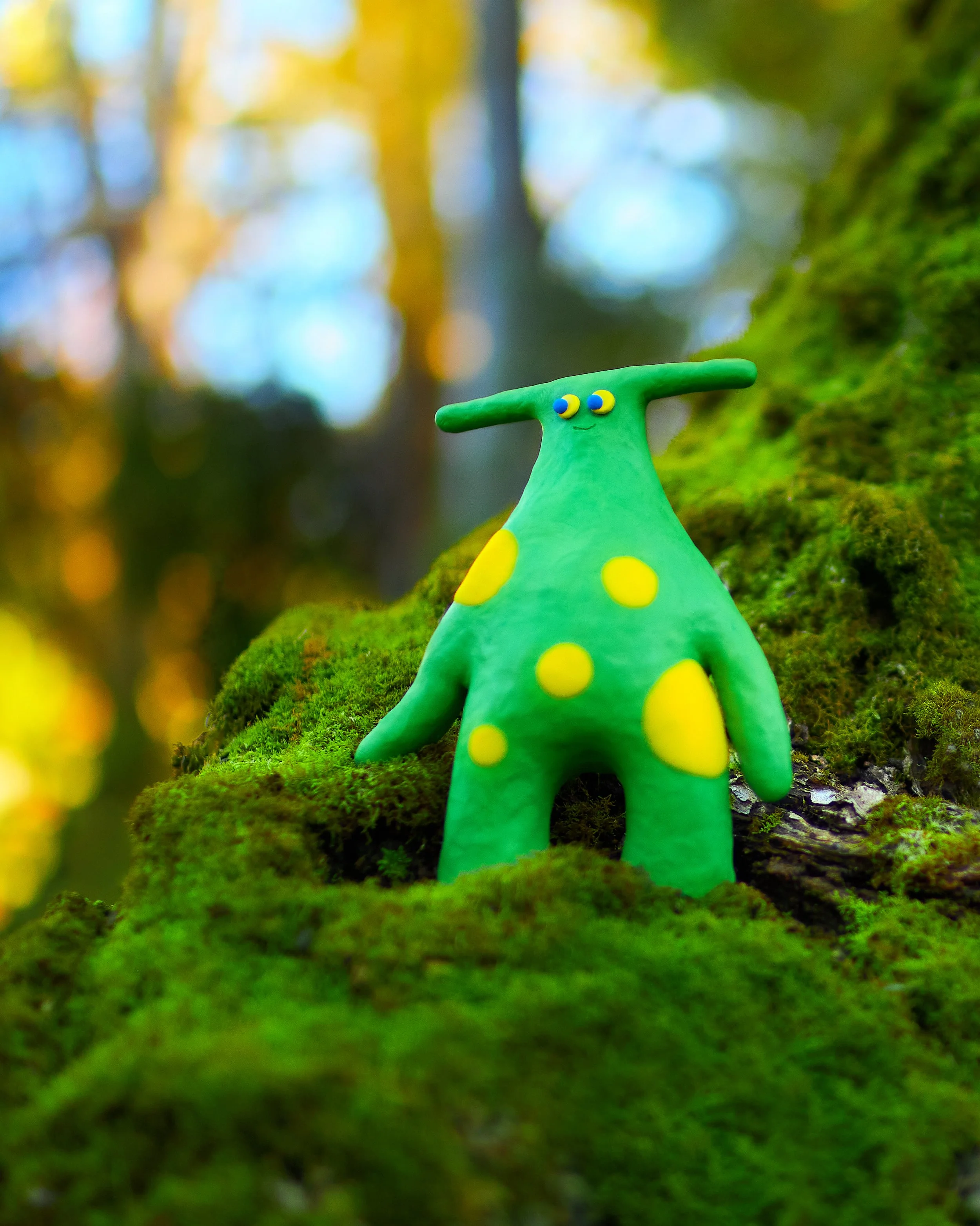 The Pit Pat Fori, standing on a moss-covered tree trunk in a forest setting with out of focus trees and sunlight in the background.