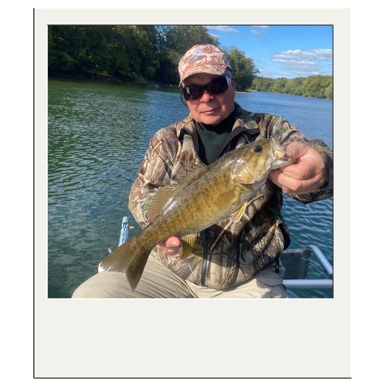 Angler in camo jacket holding smallmouth bass during a scenic river float with White Fly Outfitters.