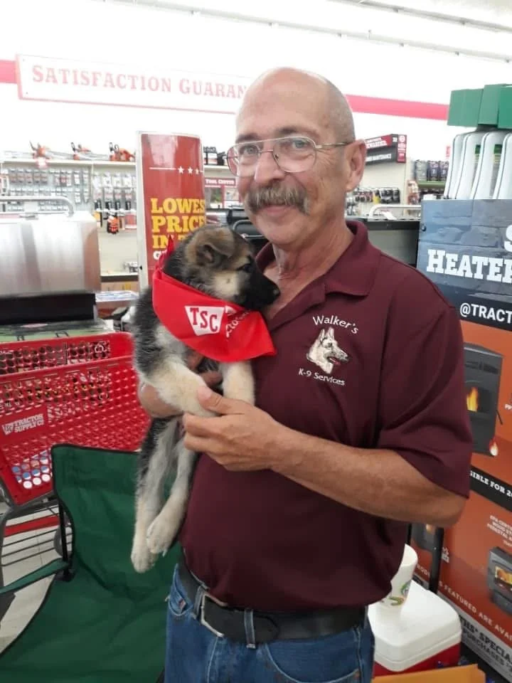A man holding a puppy at a hardware or outdoor store, with shelves of tools and equipment in the background.