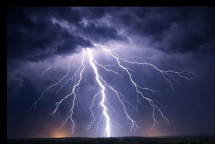 Multiple lightning bolts striking across a dark stormy sky over a flat landscape.
