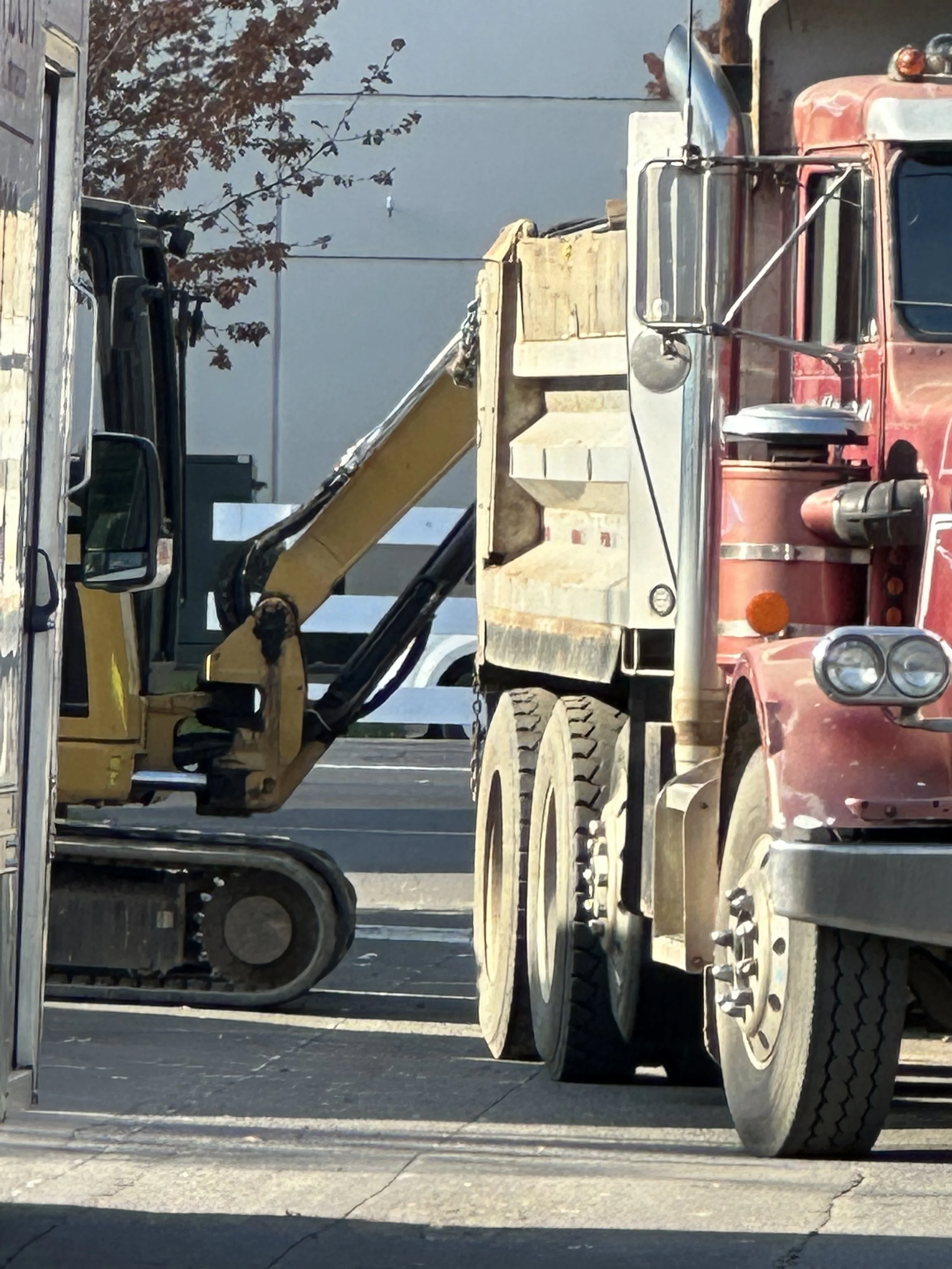 A red semi-truck and a yellow excavator parked next to each other on a street.